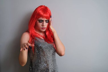 Gri arka planda kırmızı peruk takan transseksüel bir adamın portresi. LGBTQ eşcinseli.