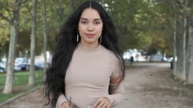 Genç Latin kız gözlüğünü çıkarıyor ve gülen yüz kamerasıyla sonbaharda sokağın ortasında..