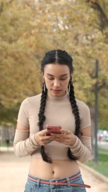 Genç Latin kız, güler yüzle akıllı telefon kullanır ve güler yüzle güler sonbaharda.
