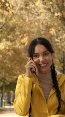 Sonbaharda sokakta akıllı telefondan konuşan gülümseyen genç Latin kız..