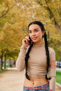 Sonbaharda sokakta akıllı telefondan konuşan gülümseyen genç Latin kız..