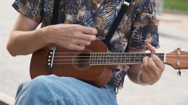 알아볼 수없는 젊은이 거리에 앉아어쿠 우쿨렐레 기타를 연주하는 — 비디오