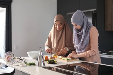 İki müslüman kadın salata hazırlamak için mutfakta sebze doğruyor, doğruyor ve soyuyorlar..