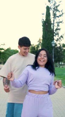 İki genç Latin arkadaş parkta dans edip gülümsüyor..