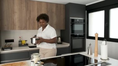 Güler yüzlü genç Kübalı kadın yemek tarifi için tencereyi indüksiyon sobasının üzerine koyuyor..