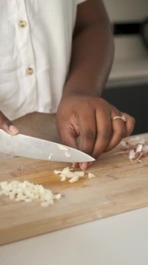 Kübalı kadın ellerine yakın çekim Bıçakla çiğ sarımsak kesiyor.