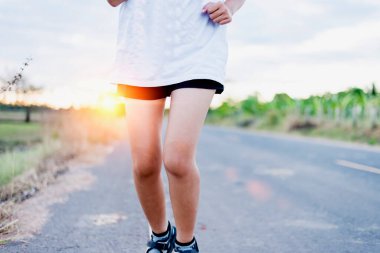 Asyalı bayan koşucu, akşam günbatımında yolda koşar.