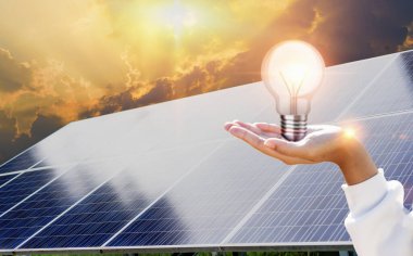 Güneş paneli arka planında beyaz bir ampul tutan bir kadın. - Evet. Güneş panelleri ve enerji tasarrufu lambaları. Temiz enerji kavramı.