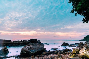 Deniz dalgaları taştan kumsaldaki kayaların üzerine düşüyor.