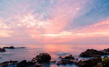 Deniz dalgaları taştan kayaların üzerine düşüyor. Gün batımı.