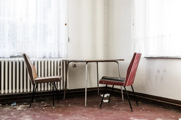 Leerer Tisch und zwei Stühle in einem chaotischen Raum — Stockfoto