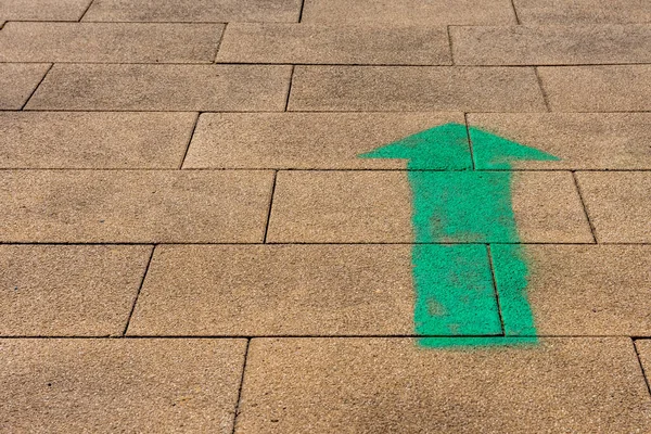 a green arrow on a footpath with direction upwards in the sunshine