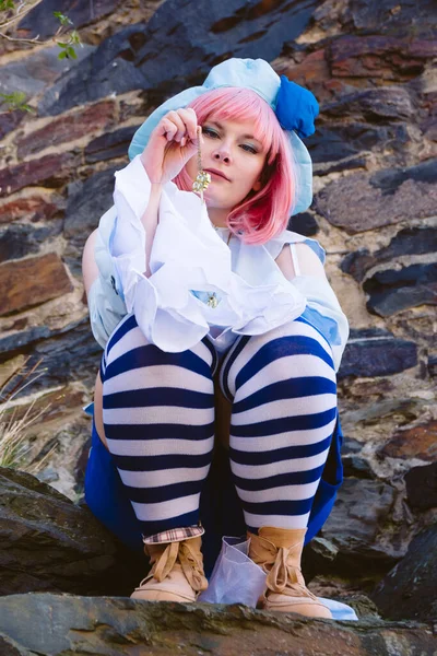 Anime karakteri gibi giyinmiş güzel bir kadın elinde anahtarla bir kayanın üzerinde oturuyor.