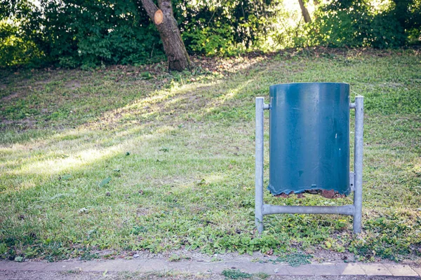 Şehir parkında eski mavi bir çöp kutusu.