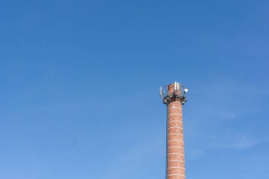 Arka planda mavi gökyüzü olan radyo ekipmanlı bir baca.