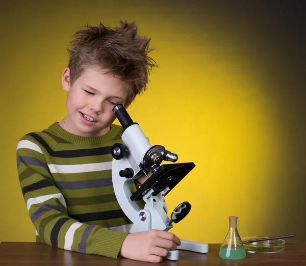 Le garçon avec un microscope et des flacons colorés sur un fond jaune . — Photo