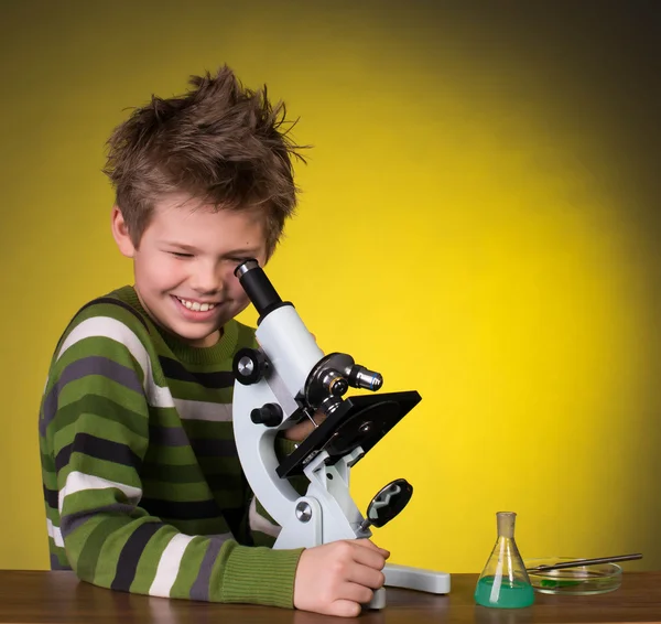 The boy with a microscope and colorful flasks on a yellow background. — Stock Photo, Image