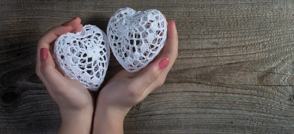 Woman hands holding white lace hearts on old wood background. Valentine's day.