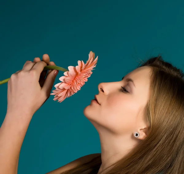 Attractive smiling woman with pink flower on blue background. — Stock Photo, Image