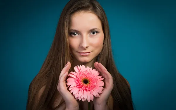 Attraktive lächelnde Frau mit rosa Blume auf blauem Hintergrund. — Stockfoto