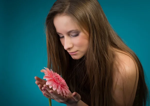 Attractive smiling woman with pink flower on blue background. — Stock Photo, Image