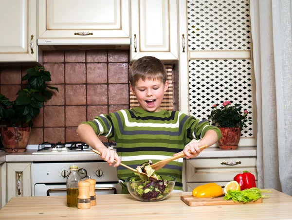 Hymyilevä poika valmistelee salaattia keittiössä. Terveellinen ruoka . — kuvapankkivalokuva
