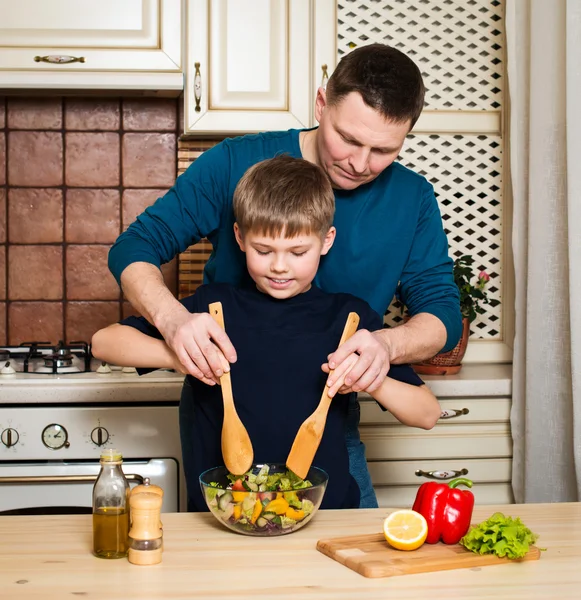 Padre e hijo preparando ensalada de verduras en la cocina . — Foto de Stock