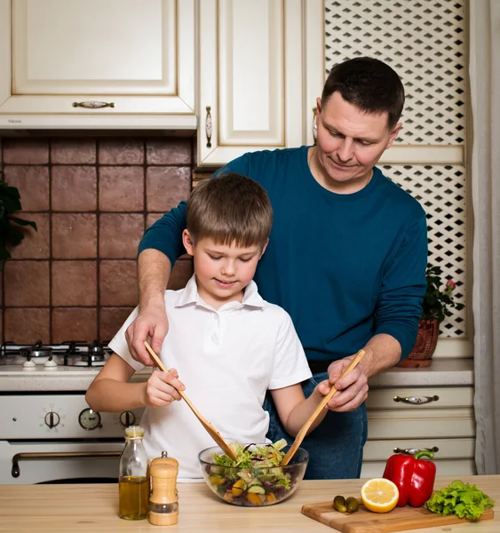 Far och son förbereder grönsakssallad i köket. — Stockfoto
