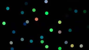 Siyah arka plandaki dekoratif çelenk üzerinde yanıp sönen bokeh ışıkları. Göz kırpan yeşil, mavi, kırmızı ve sarı. Kavram: Noel, Yeni Yıl, Tatil.