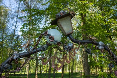 Parkland 'da bir bahar gününde yakın plan dövülmüş fener. Black Metal 'den demir sokak lambası ve ince detaylar. Mavi gökyüzüne ve yeşil ağaçlara karşı güzel bir sokak lambası. Çelik sokak lambası..