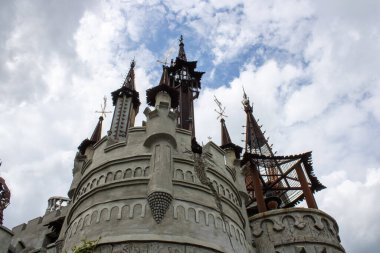 Fantezi parkındaki mistik masal şatosu. Gizemli evin mimarisinin ayrıntıları. Bulutlu havada gri taş duvarlar ve ek binanın demir çatıları. Kavram: korku ve zevk.