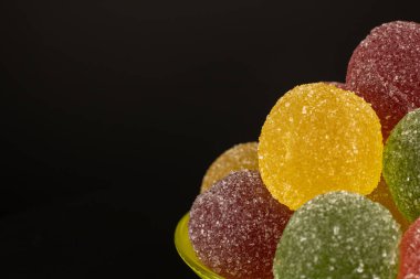 Siyah arka plandaki çay tabağındaki renkli tatlılar marmeladı. Meyve jölesi, sarı, kırmızı, pembe, üzerine şeker serpiştirilmiş. Yemek konsepti, lezzetli tatlı yiyecekler..