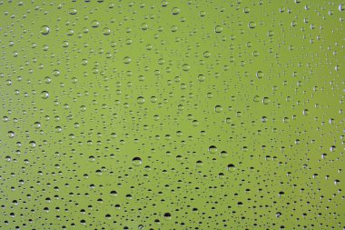 Su damlaları yeşil arka plandaki camların üzerine damlıyor. Özet arka plan