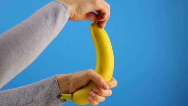 Χέρια Των Γυναικών Ξεφλουδίζουν Μια Μπανάνα Μπλε Φόντο Υγιή Κοντινό — Αρχείο Βίντεο
