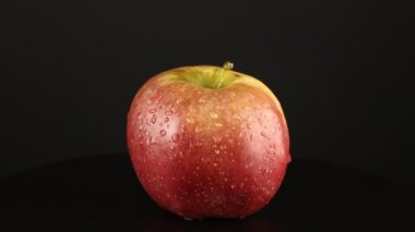 Su damlacıkları olan kırmızı elma siyah arka planda döner. Yakın çekim video vitamini.