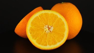 İki yarım ve bir bütün portakal siyah bir arkaplanda döner. Yakın çekim video vitamini.