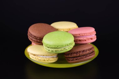 Siyah arka planda yeşil çay tabağı içinde renkli pastalar. Yemek konsepti, lezzetli tatlı yiyecekler..