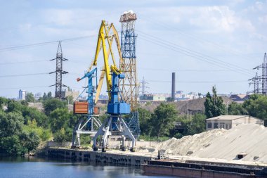 Nehirde büyük iskele vinçleri. Çıkarma ve taşıma kumu. Liman vinci su kaynaklarını mavnaya yüklüyor. Özel ekipman ve su nakliyesi. Nehir limanı. Endüstri şehri.