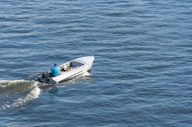 Adult man fast moving in white motorboat on the river. He drives the motor and looks for fish. Waves on the water and foam after speed. Water transport. Top view. Lifestyles.