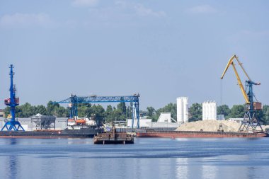 Nehirde büyük iskele vinçleri. Çıkarma ve taşıma kumu. Liman vinci su kaynaklarını mavnaya yüklüyor. Özel ekipman ve su nakliyesi. Nehir limanı. Endüstri şehri.