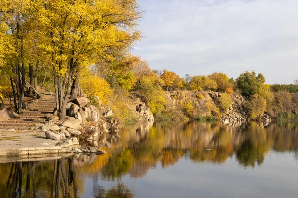 Old stone stairs in autumn. Staircase in steps among yellow foliage and big rocks. Footpath nature among lake and trees with golden leaves. Reflection of plants in calm water. Way outdoors.