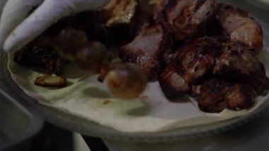 Yakın plan, şefin üzerine fırında patates koyup şişlerden çıkardığı bir tabak et gösteriyor.