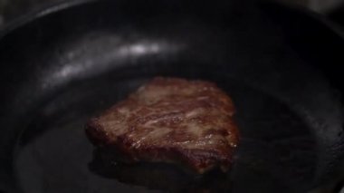 Sulu biftek tavada kızarır. Restoranın mutfağında yakın plan video çekimi. Videoda, şef bifteği maşayla çeviriyor. Kızartma tavasının kenarında bir gezegen parlıyor.