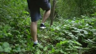 young man traveler walks along a forest path with a large hiking backpack. he is wearing gray shorts and black sneakers.