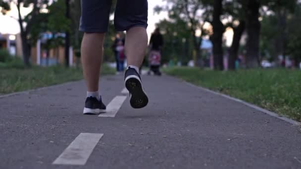 젊은이가 여름날 공원에서 조깅을 걷습니다 티셔츠와 바지를 걸치고 다리를 — 비디오