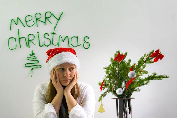 Chica joven con una camisa blanca y un sombrero rojo de Santa hizo un árbol de Navidad de ramas con decoraciones simples, un fondo simple para vacaciones minimalistas. —  Fotos de Stock