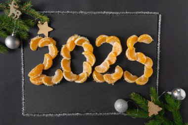 Yeni yıl 2025 yaklaşıyor. Rakamlar siyah arkaplandaki mandalina dilimleriyle sıralanmış.