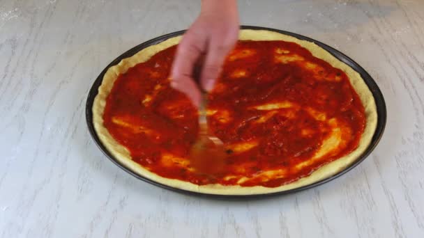 Шеф-повар покрывает тесто из сырой пиццы соусом. — стоковое видео