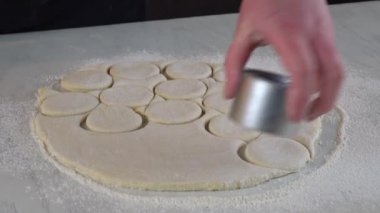 Kadın hamur çemberlerini yuvarlak küflerle kesiyor. Çörek, çörek yapmak için..