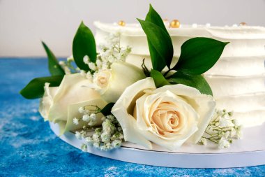 Wedding cake with white roses on blue background. Close up.